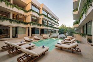 Un edificio moderno con piscina, sillones de descanso y áreas verdes en los balcones.