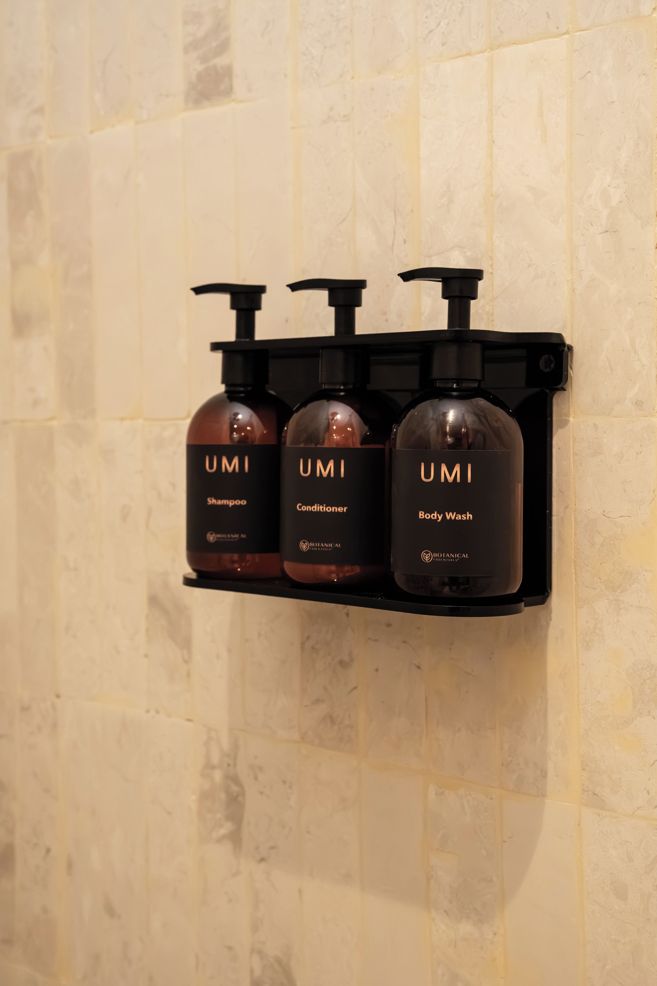 Een badkamerplankje met drie flessen van UMI: shampoo, conditioner en douchegel.