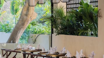 Interior de restaurante con varias mesas y sillas, lámparas colgantes y vistas al exterior con vegetación.