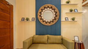 A room with a wooden door, a beige sofa, a wall-mounted mirror, and shelves with framed pictures and small plants. - Ohhana Lofts El Nido (El Nido)