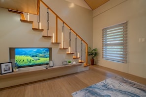 Una sala de estar moderna con una escalera de madera, un televisor de pantalla plana y un ventanal con persianas.