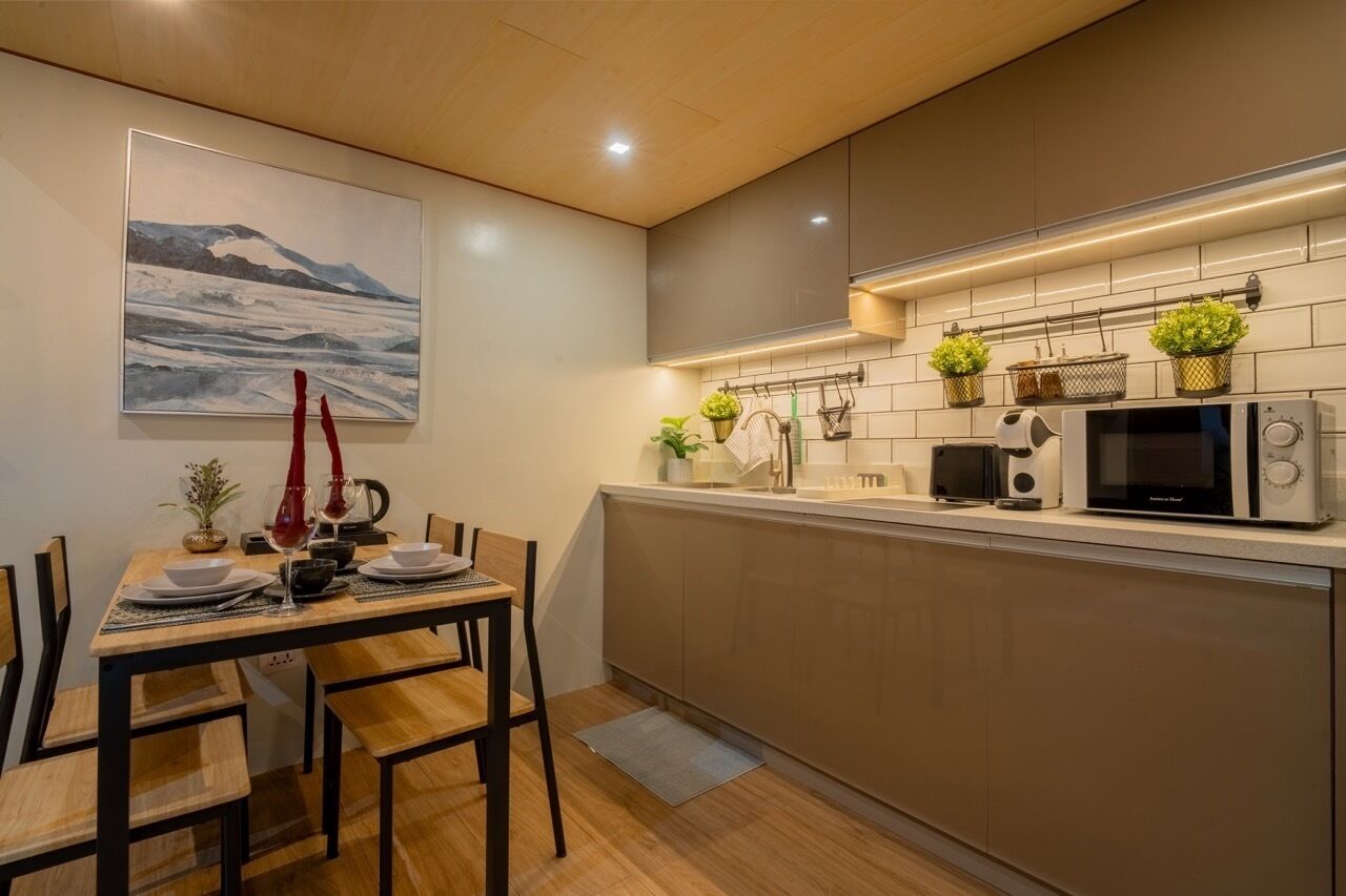 A modern kitchen with a dining area, featuring a wooden table, chairs, a microwave, and potted plants.