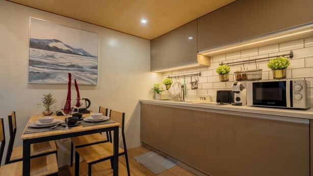A modern kitchen with a dining area, featuring a wooden table, chairs, a microwave, and potted plants. - Ohhana Lofts El Nido (El Nido)