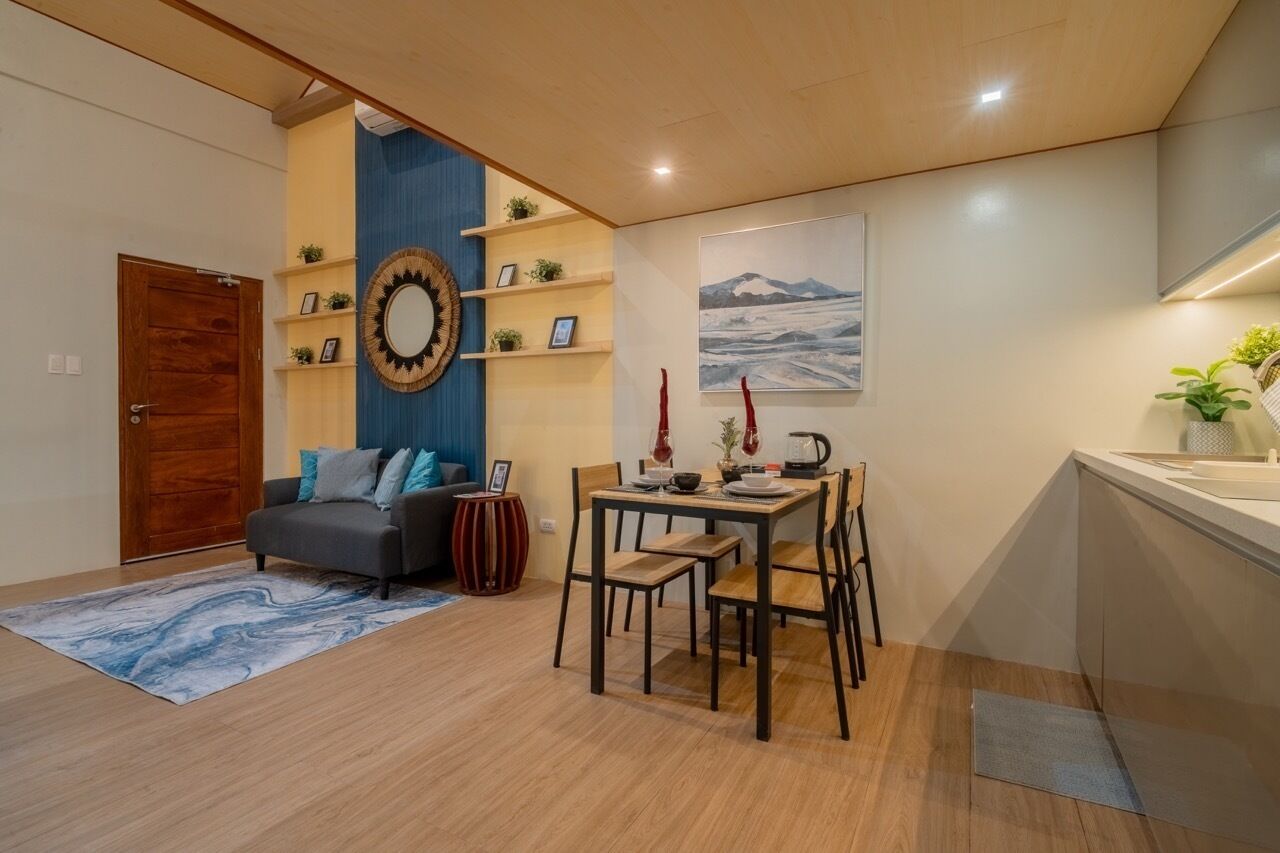 Ein modernes Wohnzimmer mit Sofa, Esstisch und Stühlen, einer Holztür und einem an der Wand befestigten Regal mit Dekoration.