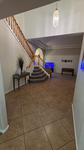A staircase with wooden railings leading to a landing, a bench, a wall-mounted TV, and a decorative hanging light fixture.
