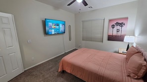 A bedroom with a bed, a TV mounted on the wall, a window with blinds, and a painting on the wall.