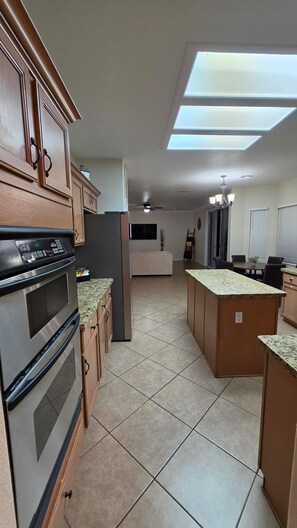 A kitchen with a built-in oven, a microwave, and a refrigerator. There is a dining area with a table and chairs. - Sunny Gilbert Retreat! Private Pool, Game Room, Golfing ⛳️ Family Fun :D (Gilbert)