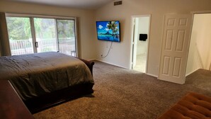 Een slaapkamer met een groot bed, een aan de muur bevestigde televisie en een deur naar een andere kamer.