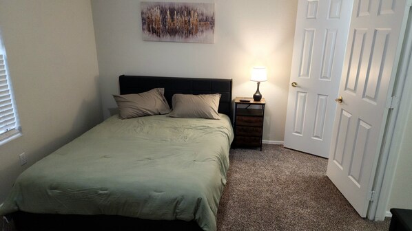 A bedroom with a bed, a nightstand, a lamp, and a door.