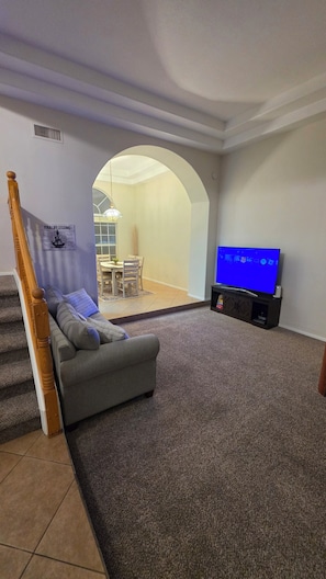 Ein Wohnzimmer mit grauem Sofa, einem Flachbildfernseher auf einem Schrank und einer Treppe mit Holzwandlaufwerk.