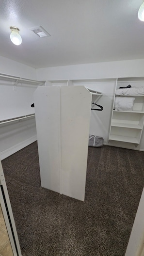 A room with a white wardrobe, a hanging rack, and a carpeted floor.
