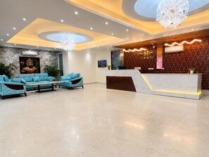 A hotel lobby with a reception desk, seating area, and a Buddha statue. - MIKADO PALACE (Gurugram)