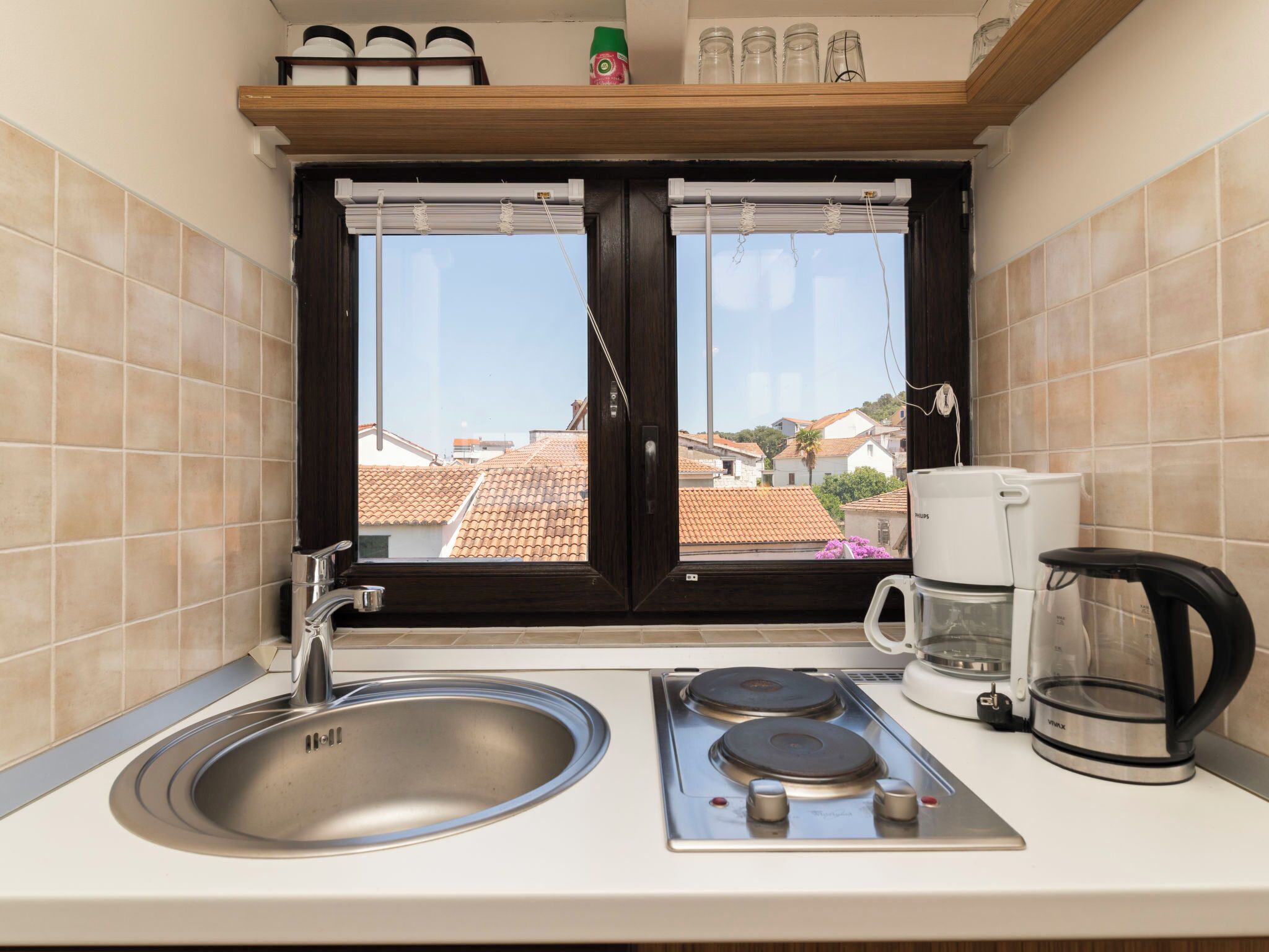 A kitchen with a window, a sink, a stove, a coffee maker, and a shelf with jars.