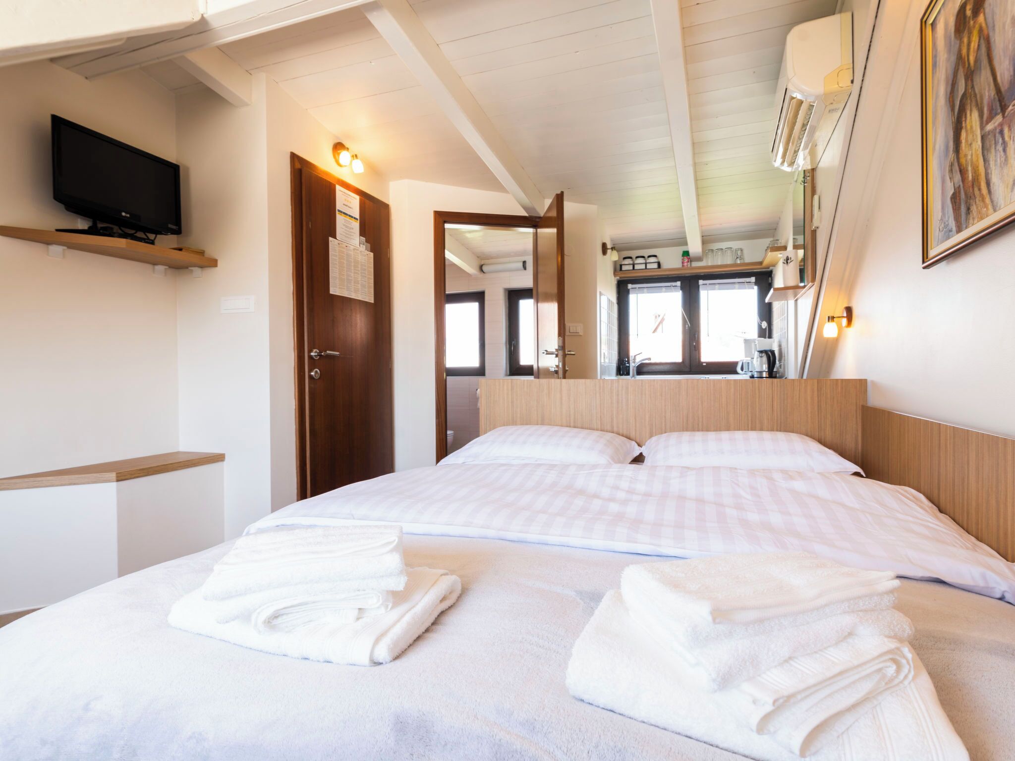 Una habitación de hotel con una cama, televisión, cabecero de madera y aire acondicionado de pared.