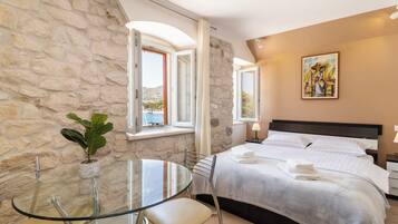 Habitación de hotel con pared de piedra, cama con ropa de cama blanca, una mesa de vidrio con sillas y un cuadro en la pared.
