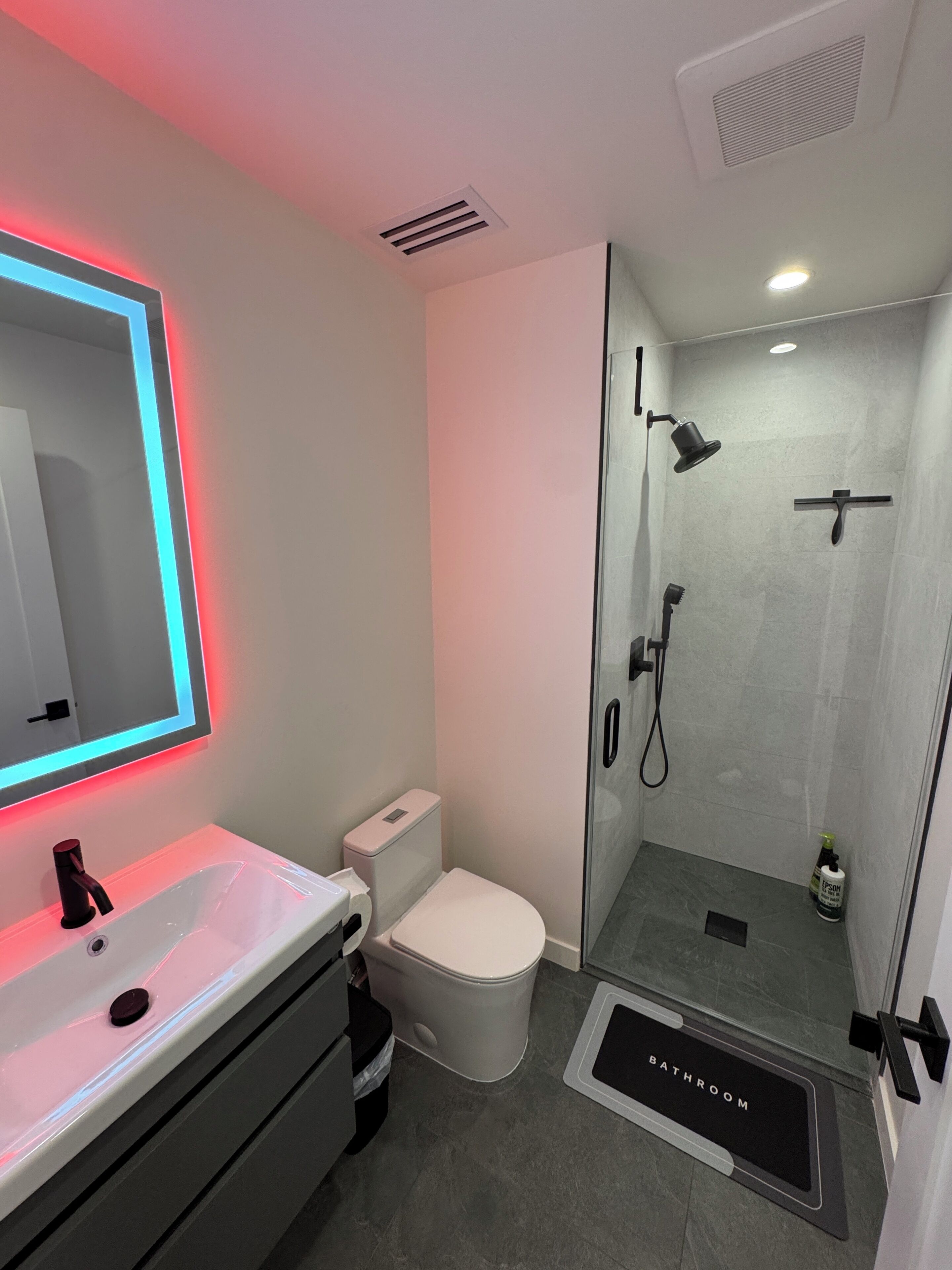 A modern bathroom with a glass-enclosed shower, a white sink with a mirror, and a toilet.