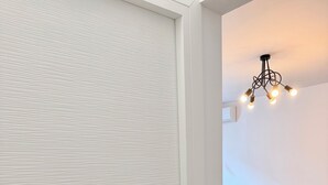 A room with a closed door, a patterned wall, a ceiling light fixture, a sofa, a rug, and a round ottoman. - Limons Apartment: Living Room and Bedroom in Downtown Bucharest (București)