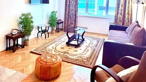A living room with a sofa, a coffee table, a TV mounted on the wall, a patterned rug, and a window with curtains. - Limons Apartment: Living Room and Bedroom in Downtown Bucharest (București)
