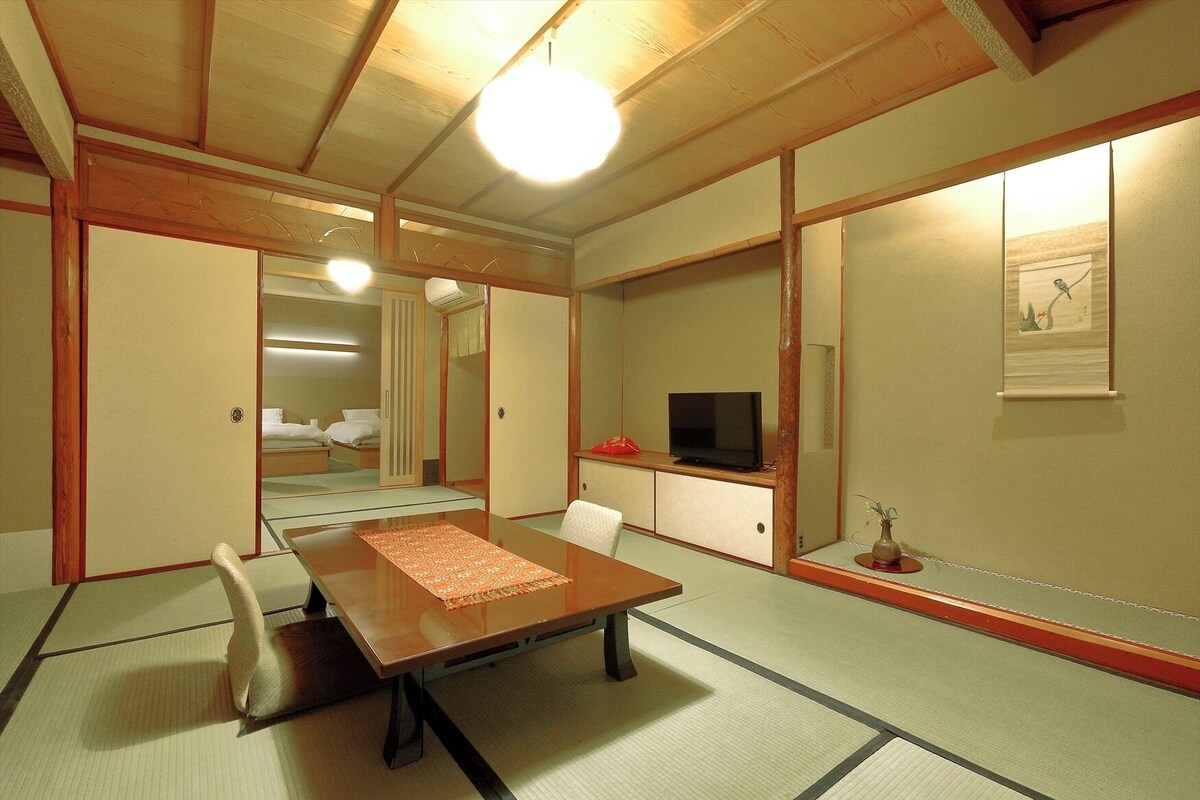 A traditional Japanese-style room with tatami flooring, a low table, a television, and a framed picture on the wall.