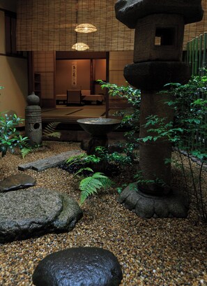A traditional Japanese garden with stone lanterns, a water feature, and a wooden interior with tatami mats. - Sumiya Ryokan (Kyoto)