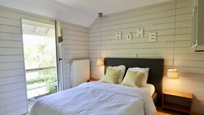Ein Schlafzimmer mit einem Bett, einem Schild mit der Aufschrift 'HOME' an der Wand, einem Heizkörper und Holzdielen.