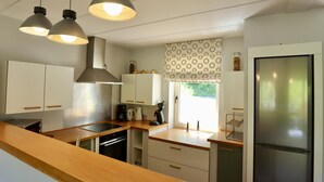Eine moderne Küche mit Pendelleuchten, einem Kühlschrank und einem Fenster mit einem gemusterten Rollo.