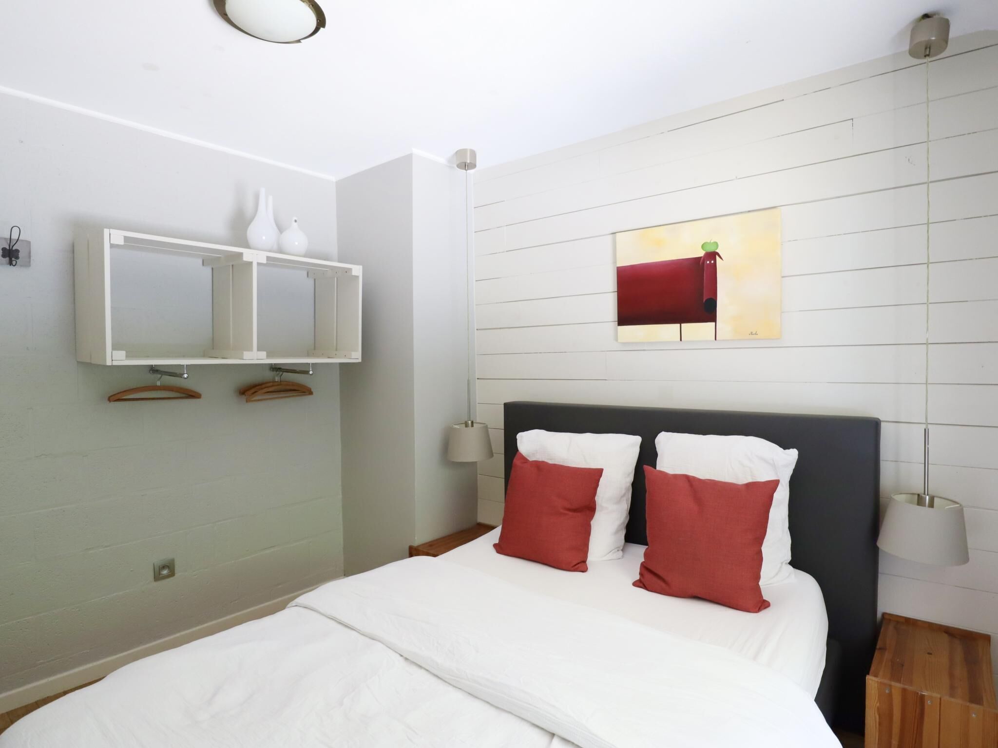 Une chambre à coucher comprenant un lit, une tête de lit, un meuble fixé au mur, une suspension et un tableau.