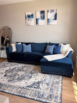 Un salon avec un canapé bleu foncé, un tapis à motifs et des œuvres d’art abstraites accrochées au mur.