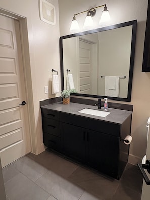 Une salle de bain avec un meuble-lavabo foncé, un grand miroir et un porte-serviettes.