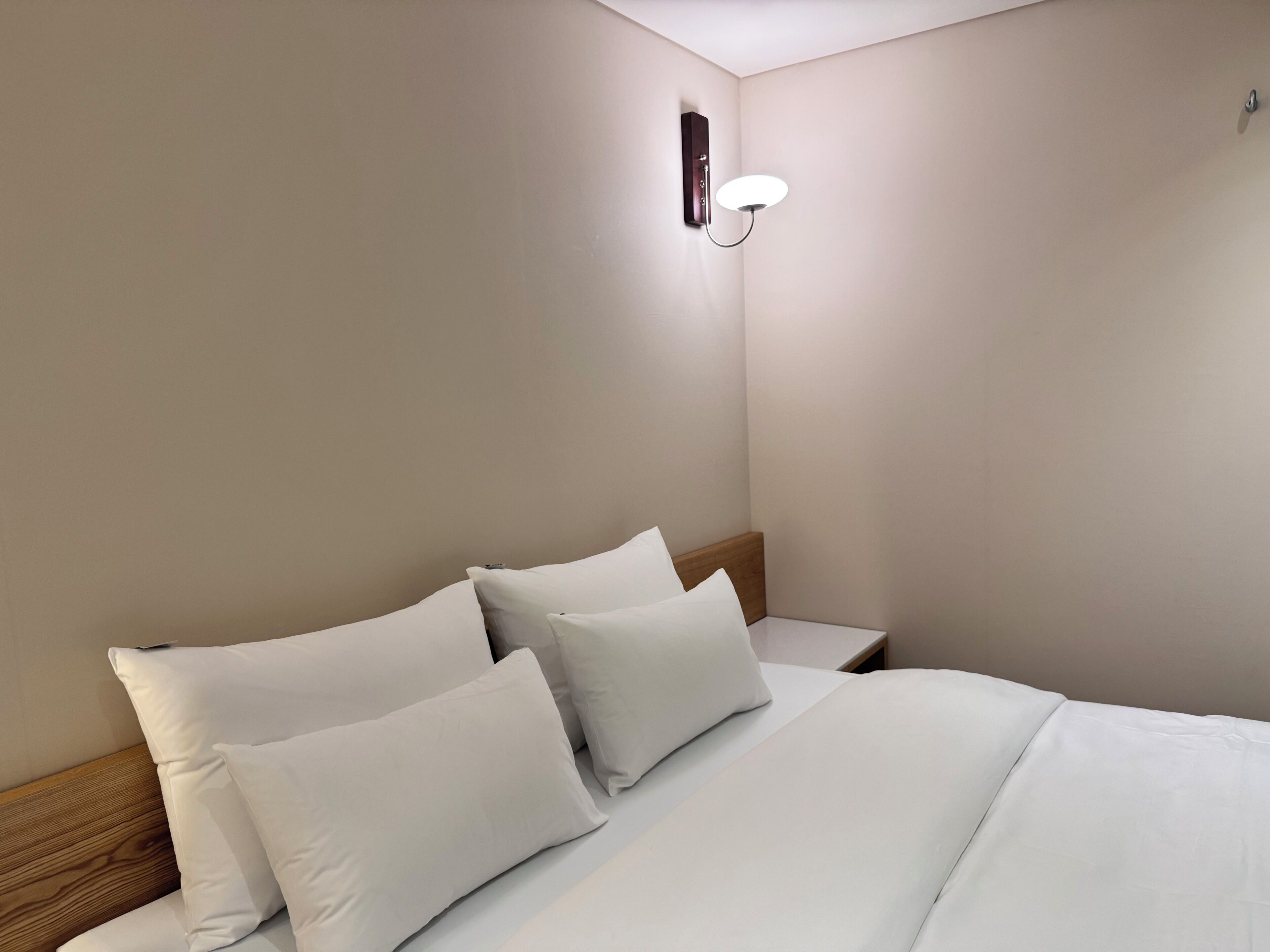 A hotel room with a neatly made bed, a nightstand, and a wall-mounted light fixture.