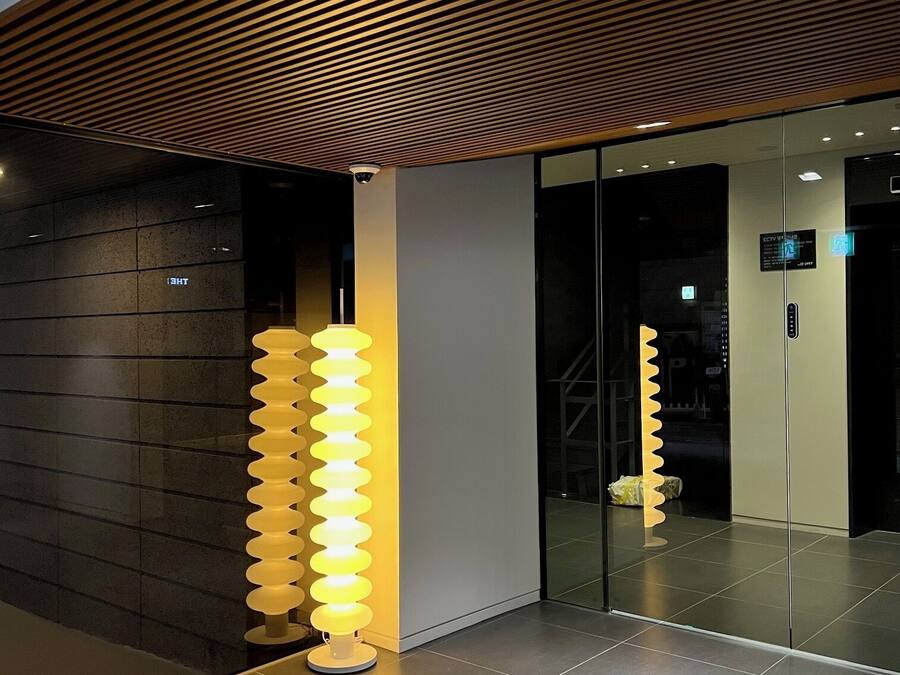 Un interior moderno con techo de listones de madera, un ascensor de vidrio y una lámpara espiral original.