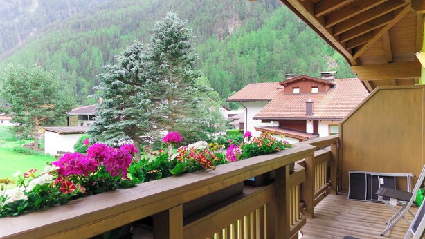 Eine Holzdar Terrasse mit Geländer, mit Blick auf eine gebirgige Landschaft mit Häusern und einem mit Schnee bedeckten Baum.