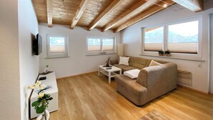 Ein modernes Wohnzimmer mit Holzbalken, einer Couch, einem Couchtisch und einem an der Wand montierten Fernseher.