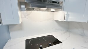 A kitchen with white cabinets, a stainless steel range hood, and a black induction cooktop. - Cute Totoro theme Tiny House (Rowland Heights)