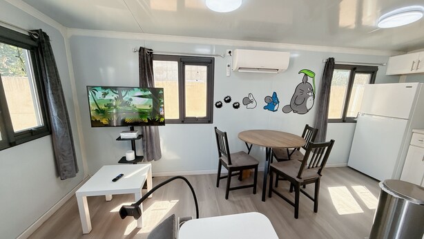 A compact living space with a TV, dining table, chairs, a sofa, a kitchen area, and a trash bin. - Cute Totoro theme Tiny House (Rowland Heights)