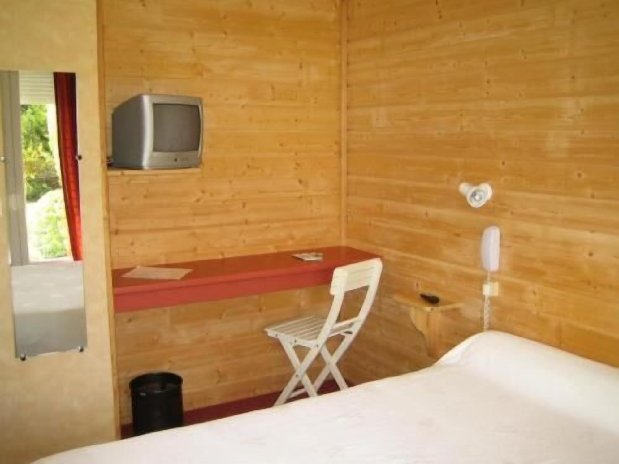 Una habitación de cabaña de madera con cama, escritorio, silla, televisor y ventana.