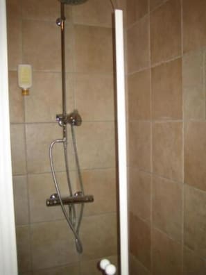 A shower with a handheld showerhead, a wall-mounted faucet, and a handheld soap dispenser.