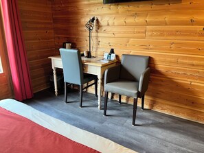 Ein Zimmer mit einer Holzwand, einem Schreibtisch mit Stuhl, einem Bett mit rot-weiß gestreifter Decke und einer Lampe.