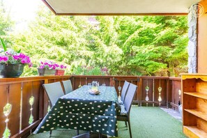 Eine Terrasse im Freien mit einem für zwei Personen gedeckten Tisch, umgeben von Stühlen und einem Holzzaun.