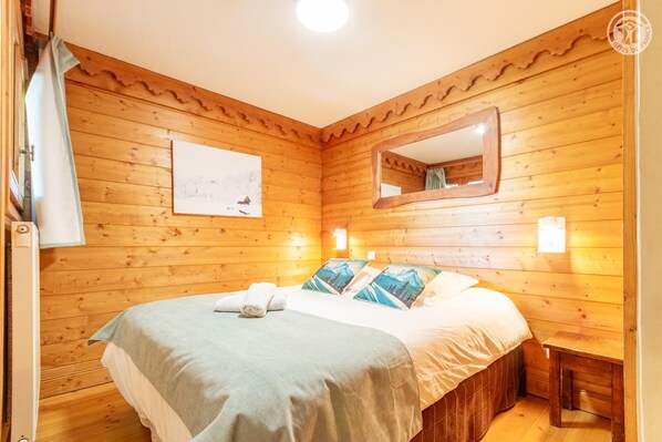A wooden-paneled room with a bed, a mirror, and a wall-mounted light fixture.