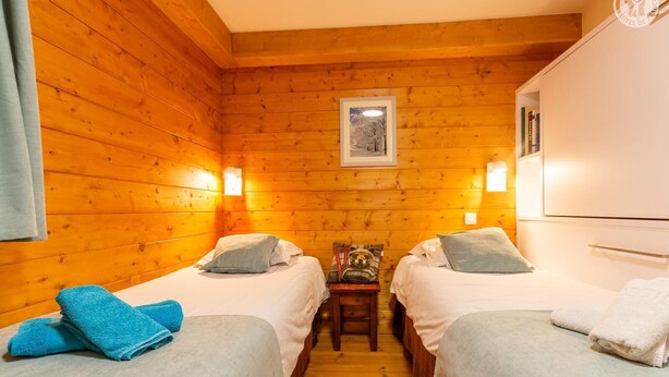 Ein Zimmer mit zwei Betten, Holzwänden, einem kleinen Tisch und einem gerahmten Bild an der Wand.