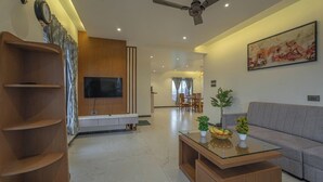Un salon moderne avec un téléviseur à écran plat, un canapé gris, une table basse agrémentée de plantes et, au fond, un coin repas.