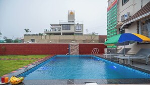 A swimming pool with a red brick wall, a small waterfall feature, and a few lounge chairs.
