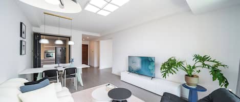Una sala moderna con sofá, mesa de centro, televisor, zona de comedor y cocina al fondo.