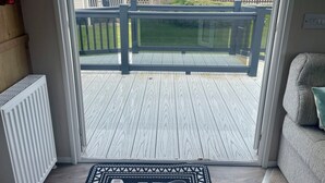 Une pièce avec vue sur une terrasse en bois, un radiateur blanc et un canapé gris.
