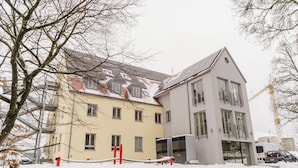 A building with a yellow facade and a grey one, both with multiple windows and a flat roof.