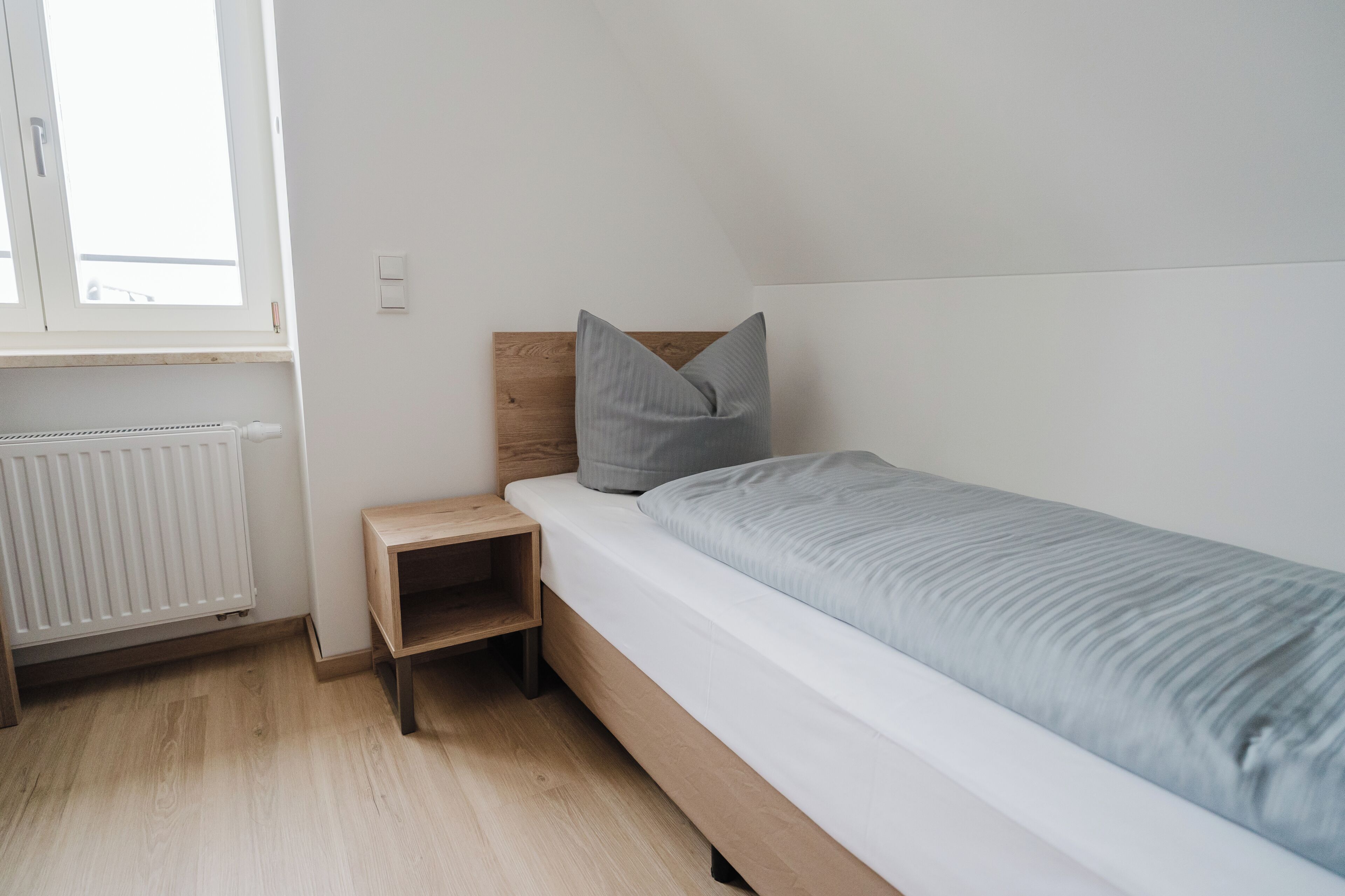 Un lit simple avec une tête de lit en bois, une table de chevet et un radiateur.