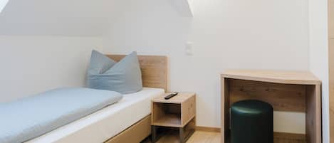 Une chambre à coucher avec un lit, une table de chevet, un bureau et une poubelle.