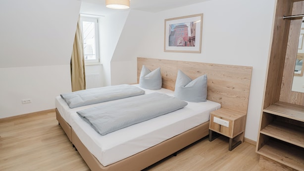 A modern bedroom with a wooden headboard, a large bed with two pillows, a nightstand, and a wooden shelf.