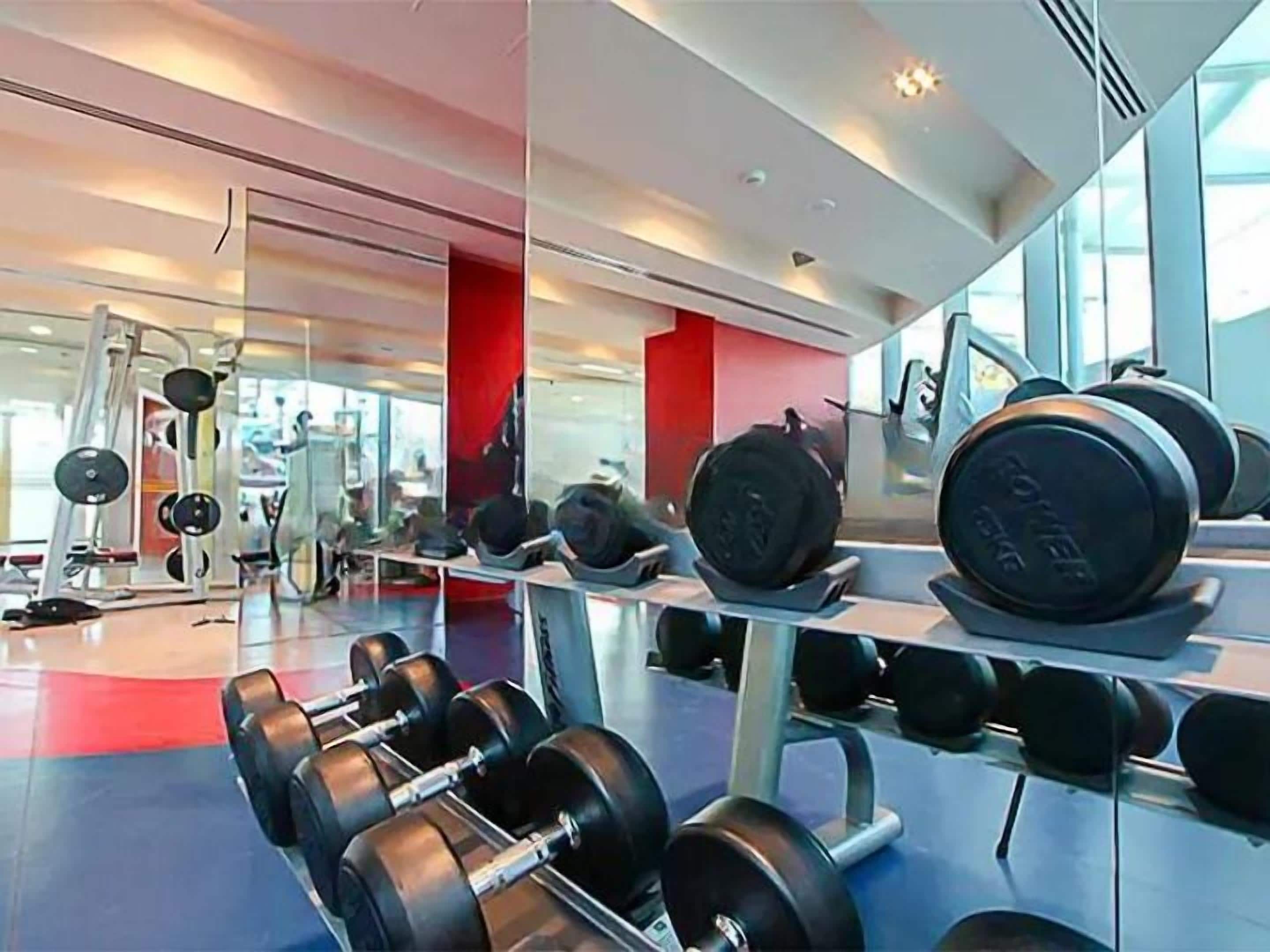 Une salle de sport équipée de matériel de musculation, notamment des haltères et des barres, et dotée d’un mur recouvert de miroirs.